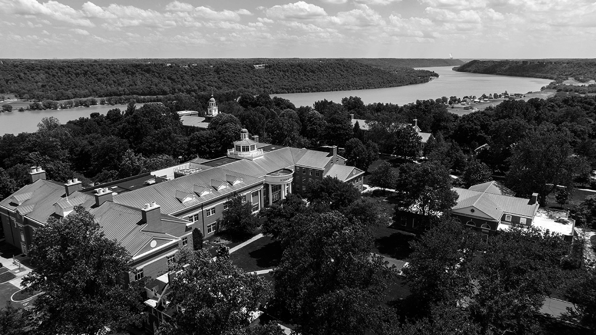 Aerial view of a large building with trees and a river in the background